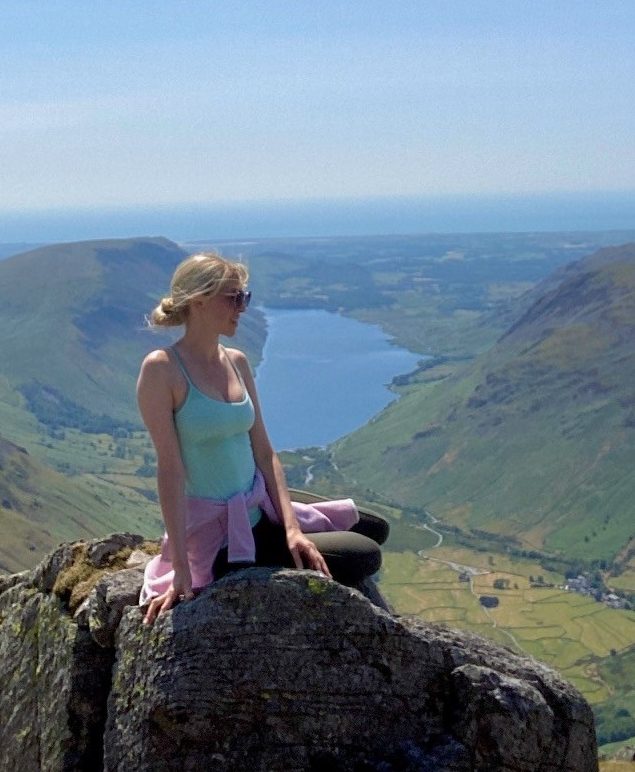 Girl sitting on a rock up a mountain in the Lake District with a lake in the background