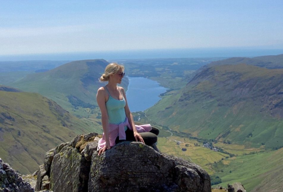 Girl sitting on a rock up a mountain in the Lake District with a lake in the background