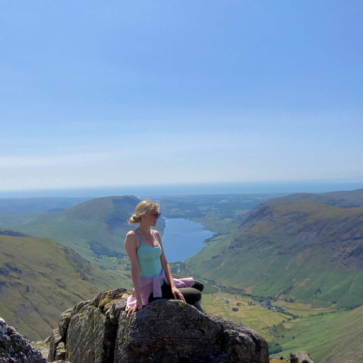 Girl sitting on a rock up a mountain in the Lake District with a lake in the background